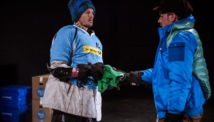 Stadttheater Zwei dick eingepackte Menschen mit Mützen und mehreren Schichten Kleidung übereinander zerren an einem Kleidungsstück.