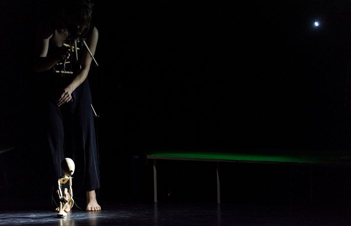 citizenpark_2 Eine Person im Dunklen beim Marionettenspiel. Nur die Holzmarionette ist hell angestrahlt.