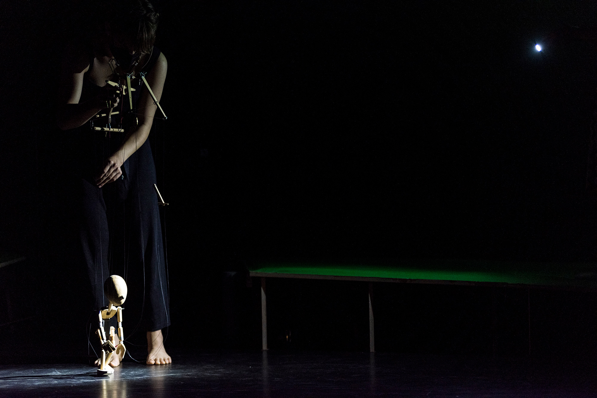 Eine Person im Dunklen beim Marionettenspiel. Nur die Holzmarionette ist hell angestrahlt.