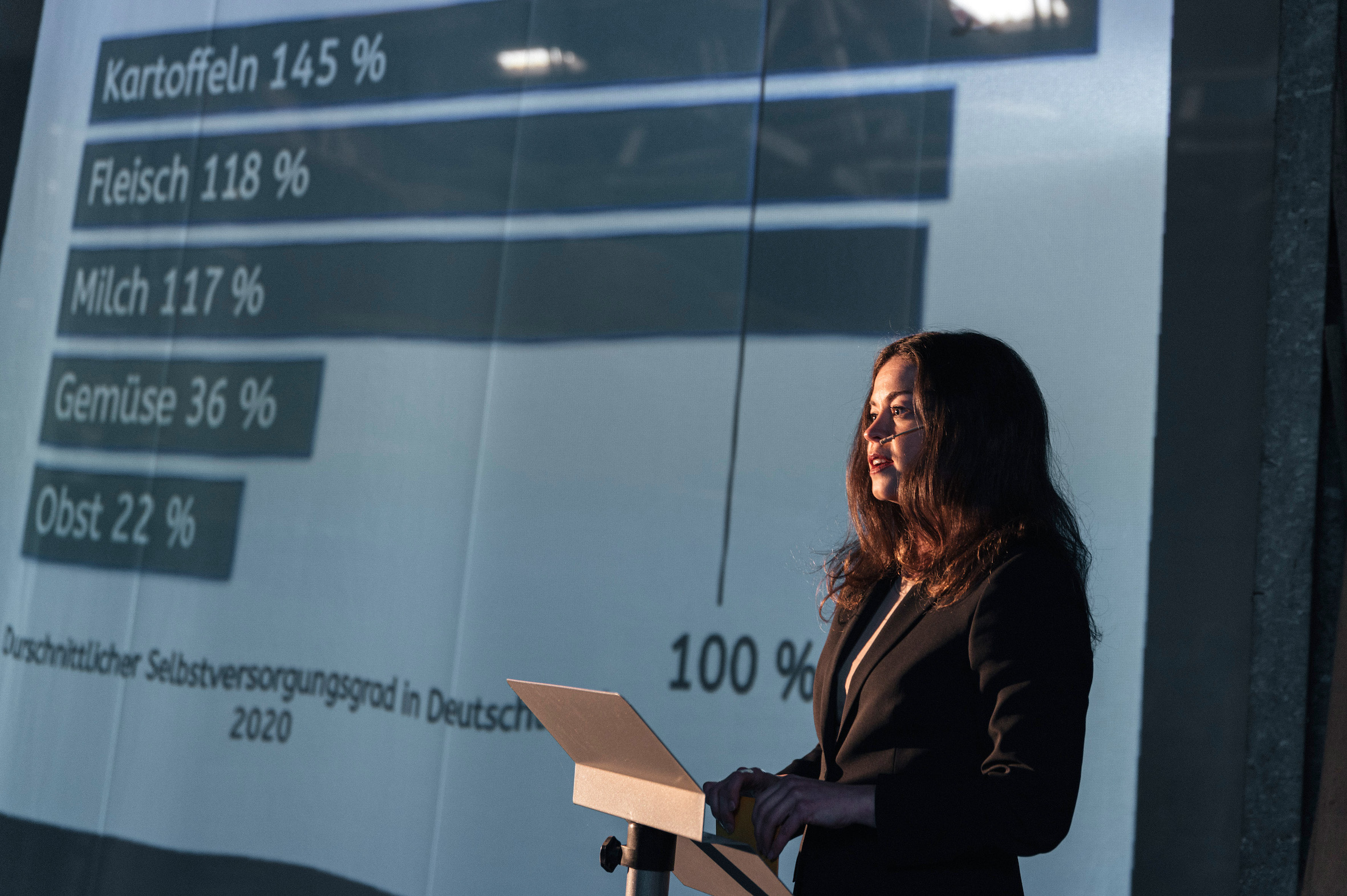 Eine junge Frau hält einen Vortrag vor einer Leinwand mit statistischen Zahlen.