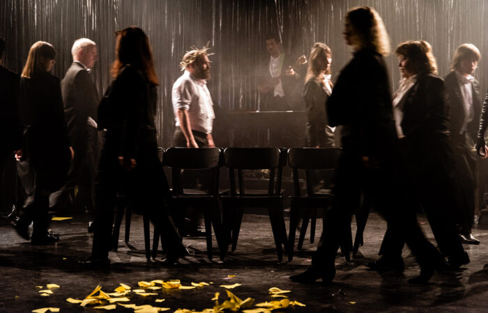 JudenJudenJuden-IsabelMachadoRios-7324_web Im Frack gekleidete Menschen spielen "Reise nach Jerusalem". In der Mitte stehen leere Stühle. Eine Person trägt ein weißes Hemd und eine Dornenkrone.