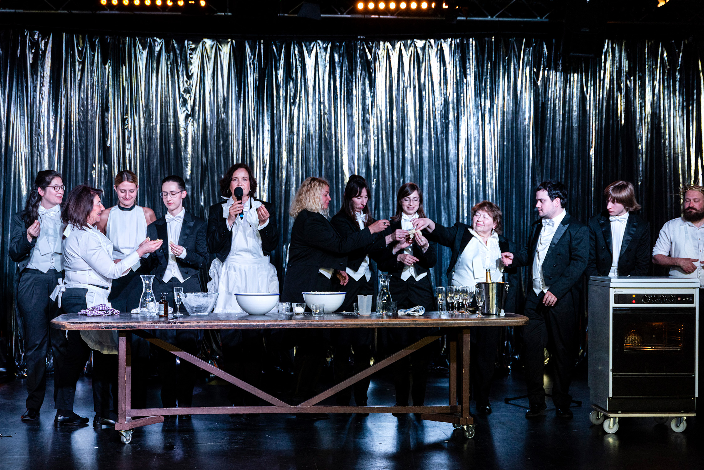 Zwölf festlich gekleidete Personen stehen hinter einem Tisch. Darauf Schüsseln, Sektkühler und Sektgläser.